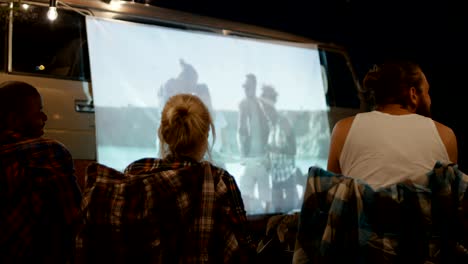 friends watching movie on screen in campsite