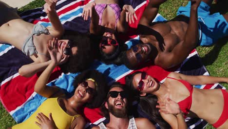 diverse group of friends sunbathing together smiling and waving to camera