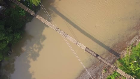 aerial headshot of suspension bridge over the river with motorcycle crossing on it in the foggy morning with sun ray, indonesia