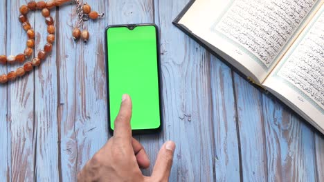 man hand using smart phone and holy book quran on table