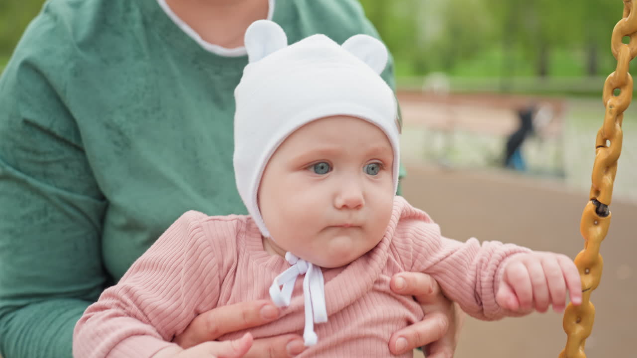 Child In Hat Held Tenderly, Caucasian Grandmother Comfortingly Holds Baby In Peaceful Park Scene, Soft Background Shows Gentle Protectiveness As Grandmother Embraces Infant With Care And Love