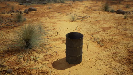 Metal barrel on dry desert ground surrounded by sparse vegetation