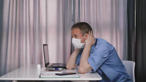 overstrained doctor sits at table with laptop in hospital