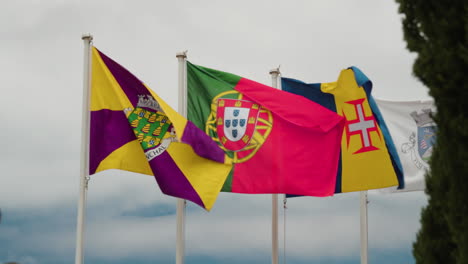 flags of funchal city, madeira island, and portugal swaying on gentle breeze. wide shot