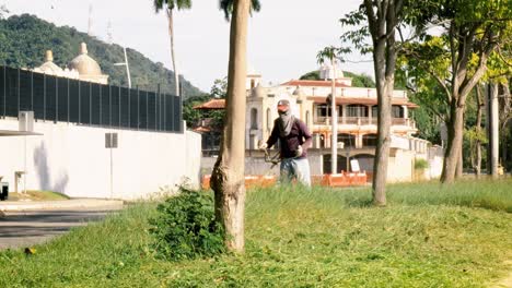 Trabajador-Público-Vestido-Con-Ropa-Protectora,-Operando-Una-Máquina-Cortadora-De-Césped-Para-Dar-Mantenimiento-Y-Embellecer-La-Apariencia-Del-Paseo-Del-área-Pública,-Calzada-De-Amador,-Ciudad-De-Panamá