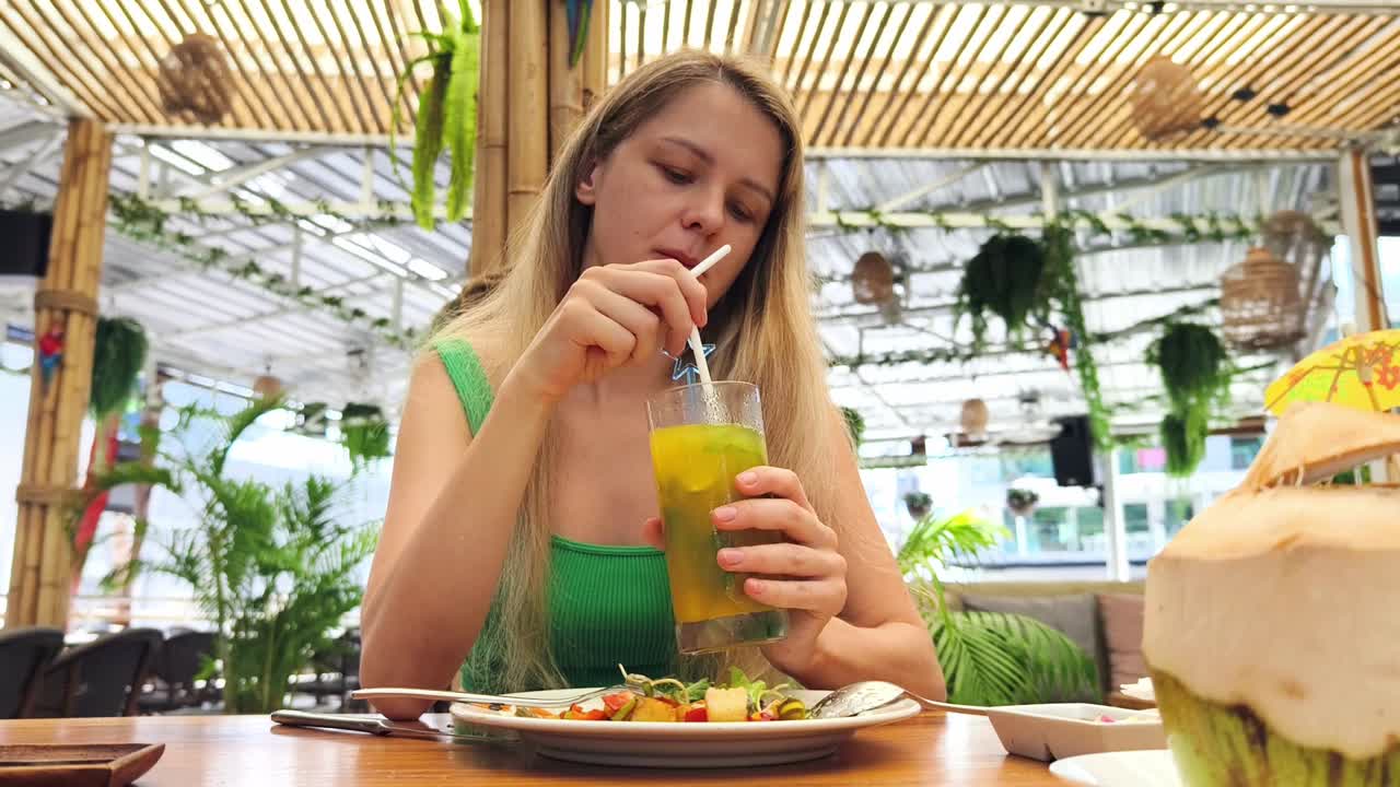 mujer disfrutando de una bebida refrescante y una comida ligera en un restaurante tropical al aire libre