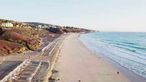 Sandy-shore-of-Fuerteventura-with-waves-gently-washing-up,-few-people-scattered-along-the-beach,-serene-vibe,-aerial-view