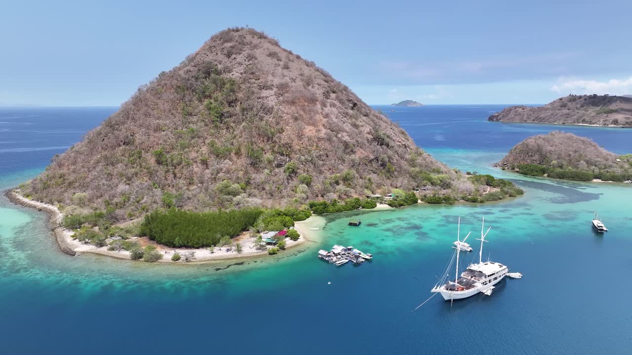 Labuan bajo, waecicu beach in indonesia, featuring crystal-clear waters, boats, and lush hillside, aerial view