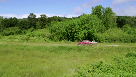 red vehicle drives on the middle of green field beside the lush forest