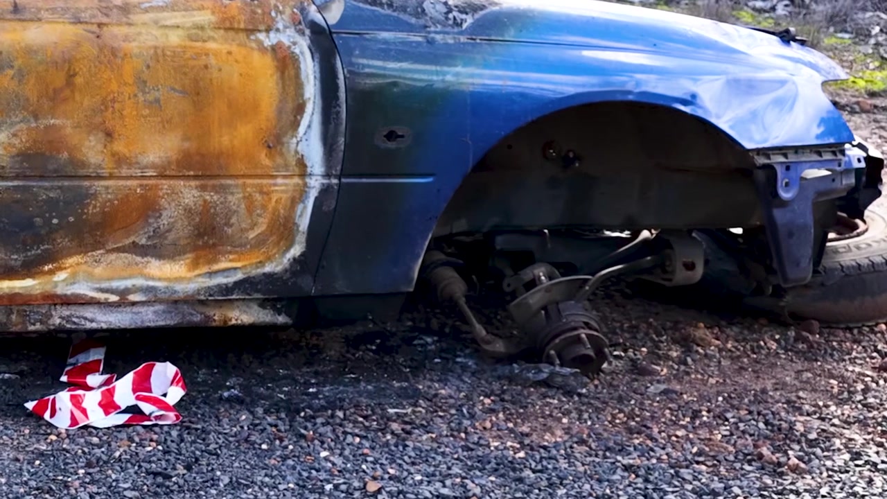 Primo piano di una berlina arrugginita e danneggiata dal fuoco, abbandonata su una strada sterrata nell'Australia rurale.