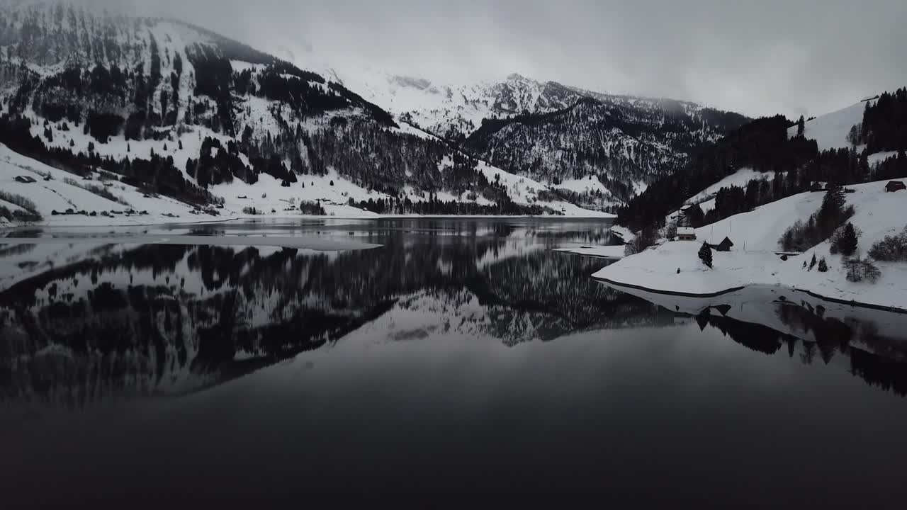 Camera flying backwards and tilting up to show the beautiful winter mountain lake panorama in Switzerland