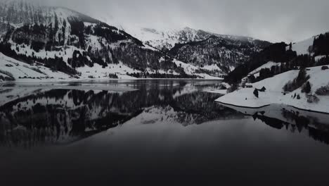 camera flying backwards and tilting up to show the beautiful winter mountain lake panorama in switzerland