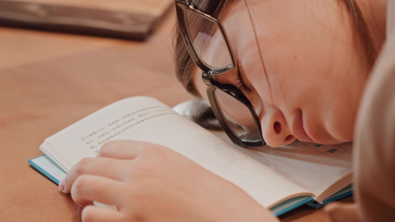 休憩中の学生がうたた寝している。学生が勉強中に静かに眠る。学生が安らかに休む静かな深夜の復習。夜、開いた本の上でうたた寝する学生がいる、穏やかで静かな作業スペース。