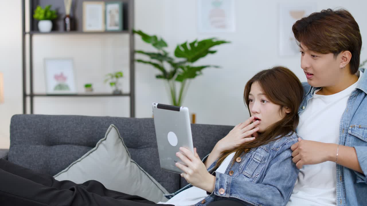 タブレットのコンテンツに驚き、ショックを受けているアジア人カップル。