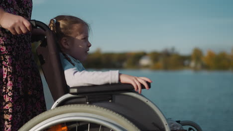 preschooler with braids sits in wheelchair on coast of lake