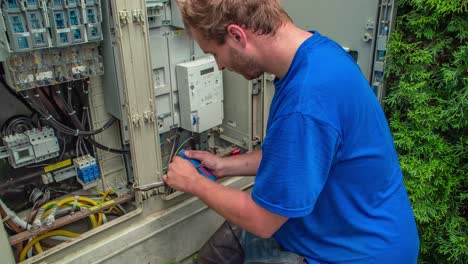 joven cortando cables eléctricos frente al armario eléctrico