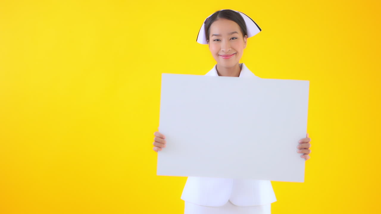 Asian smiling nurse holding a blank sheet of the paper poster banner in hands with a happy face expression