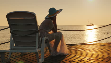 a woman looks at the sunrise over the sea sits on a sunbed in the distance a fishing boat is visible