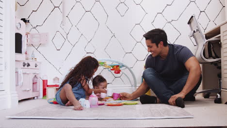 Young-girl-playing-tea-party-sitting-on-the-floor-with-dad,-and-baby-brother-beside-them