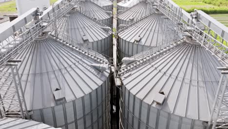 smooth low drone flight moves forward above shiny silver grain silos in latvia