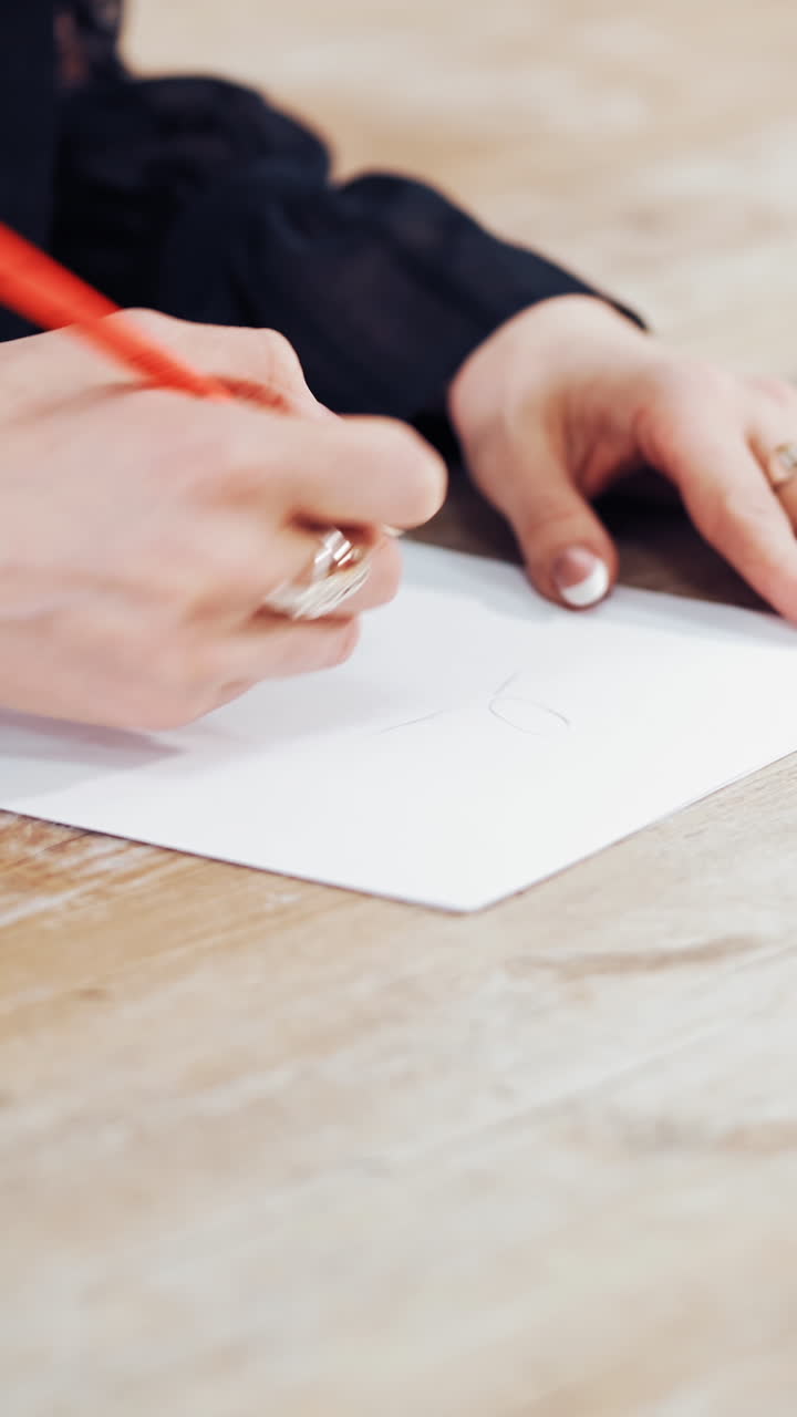 Seamstress draws a sketch of a stylish dress on the wooden background. Woman's hands are making a pattern of a future clothing with a pencil in atelier. Feminine hobby. Vertical video