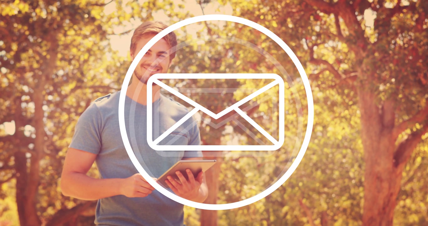 Man standing in sunlit park tapping tablet after envelope alert fading in, checking email, smiling