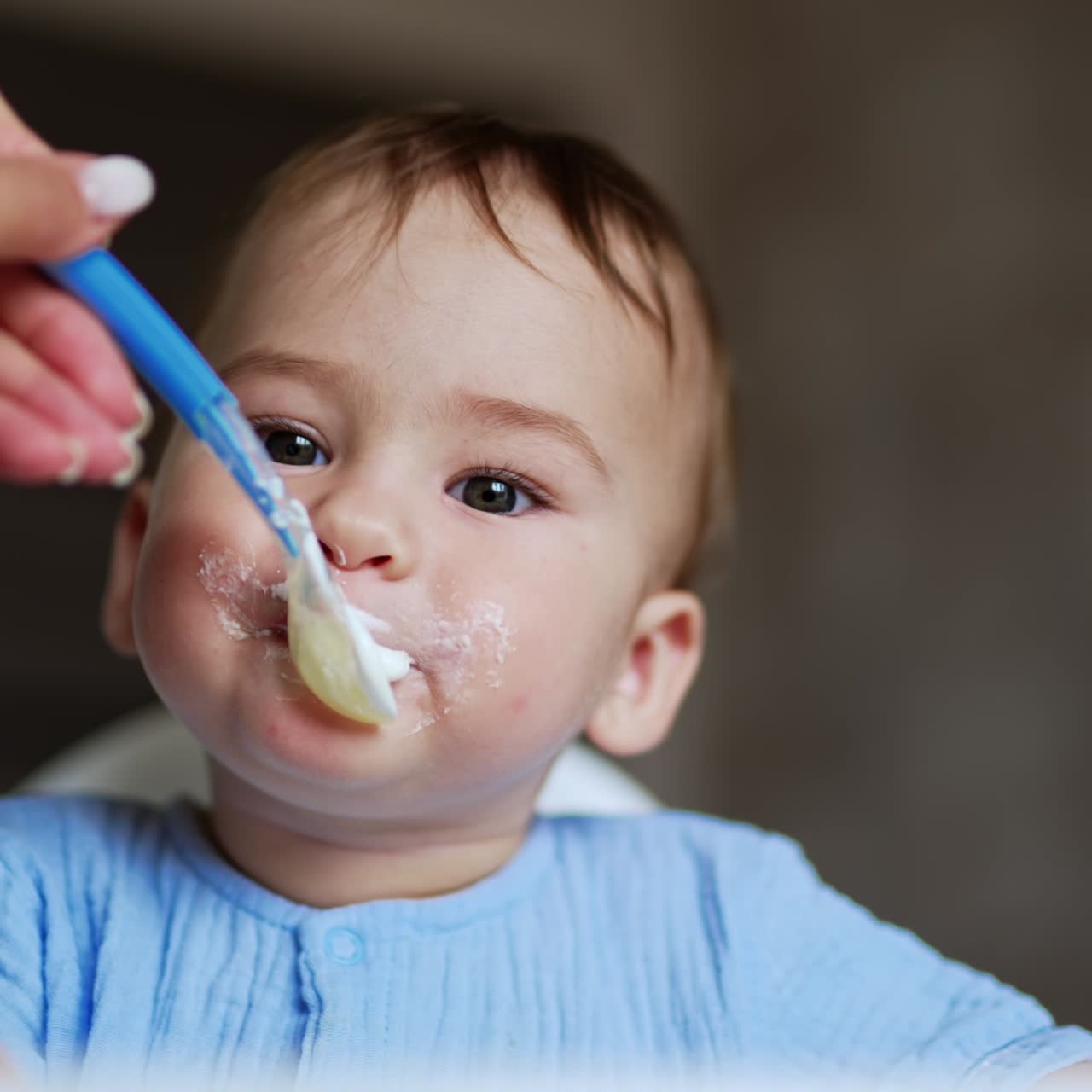Cute kid eating porridge from spoon. Mother gives porridge to baby and takes the porridge out of kid's face