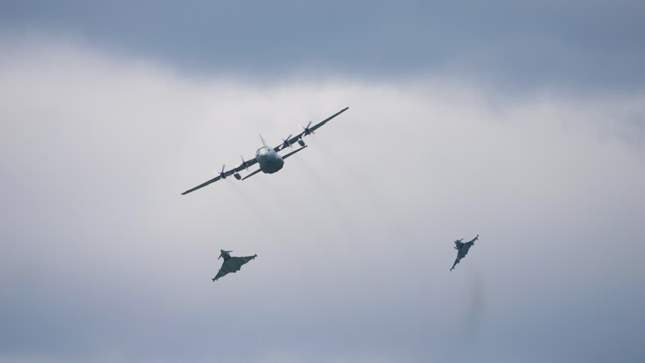 Airplane of the type Airbus A400M and the fighter aircraft types Eurofighter fly through the air with clouds in the background. The Eurofighters try to intercept the Airbus