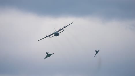 airplane of the type airbus a400m and the fighter aircraft types eurofighter fly through the air with clouds in the background. the eurofighters try to intercept the airbus