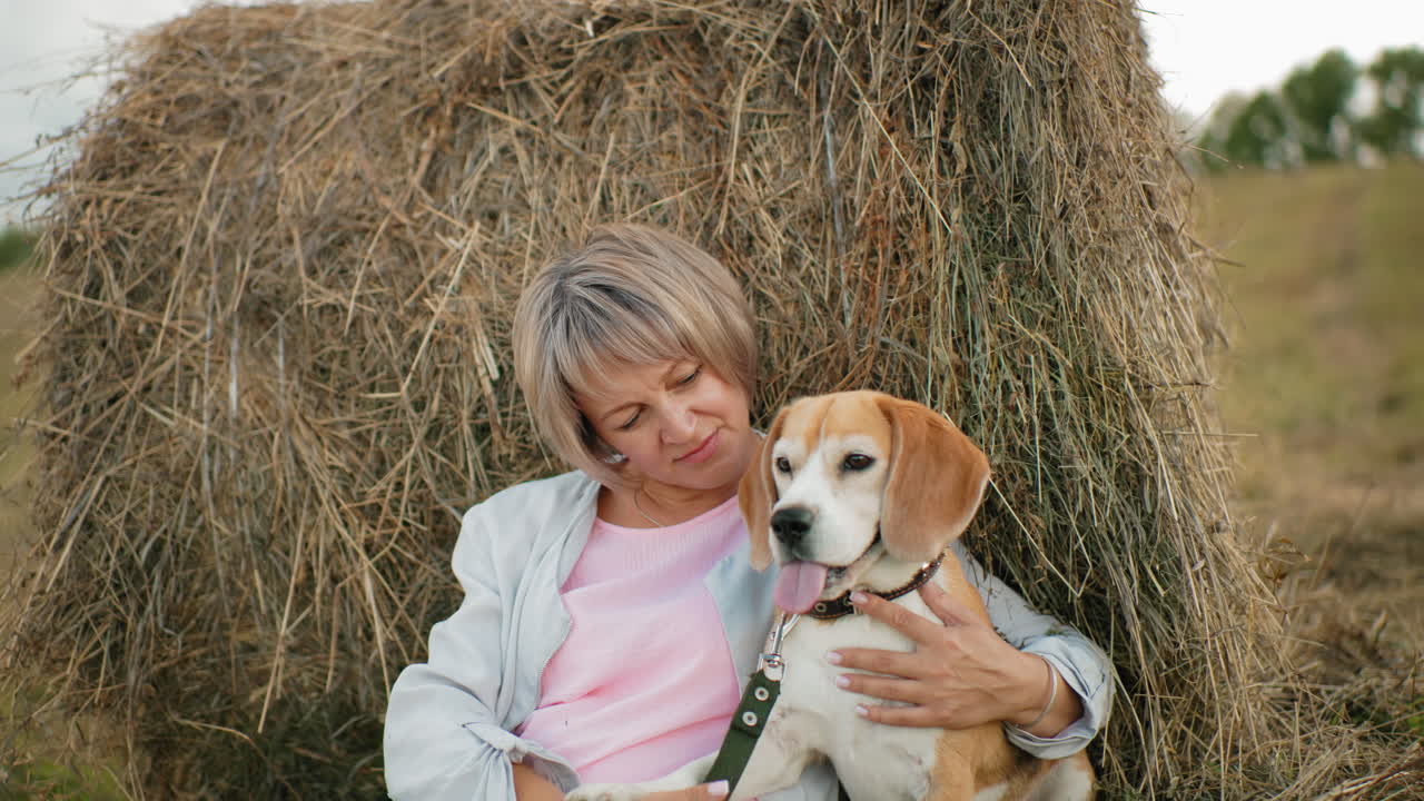 한 여자가 개를 가까이 붙잡고 애정으로 만지며, 광활한 농지에서  에 누워있는 동안, 그녀는 개를 사랑으로 바라보고, 열린 시골에서 평화롭고 친밀한 순간을 공유합니다.
