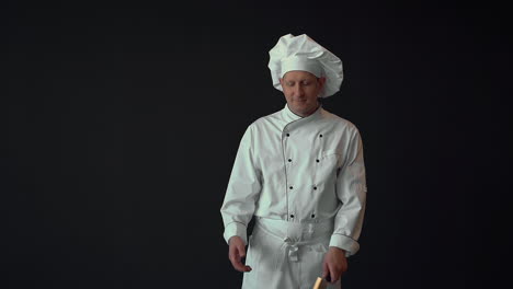 male chef checking the quality of a large sharp kitchen knife. copy space on black background.