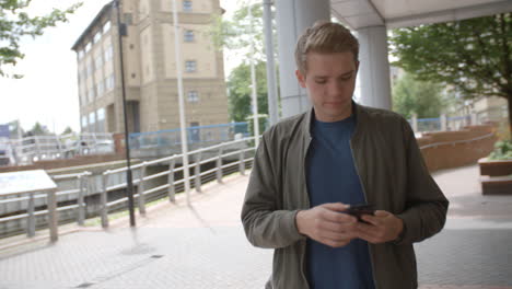 Un-Joven-Blanco-Caminando-En-Un-Entorno-Urbano-Contestando-Su-Teléfono