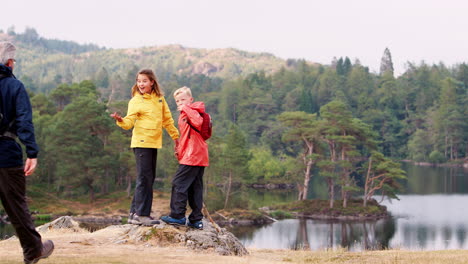 Kinder-Rennen-Ins-Bild-Und-Laden-Ihre-Großeltern-Ein,-Die-Aussicht-Auf-Den-See-Zu-Bewundern,-Rückansicht,-Seenplatte,-Vereinigtes-Königreich