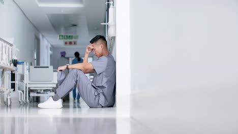 stressed asian male surgeon sitting and leaning on wall in hospital in slow motion