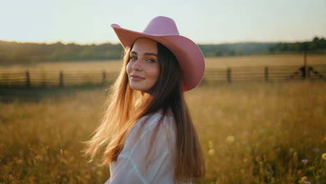 young woman in pink cowboy hat in a golden field at sunset