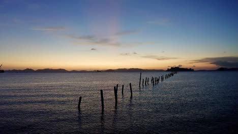 Old-wooden-dock-posts-stick-out-of-the-sea-during-sunset,-static-shot