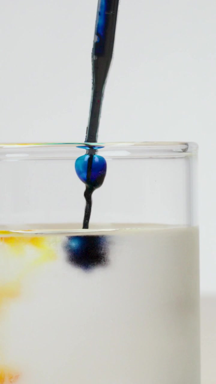 Inquadratura verticale ravvicinata di colorante alimentare blu che si diffonde in un bicchiere d'acqua limpida.