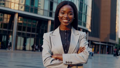 confident african american professional manager standing with arms crossed, radiating success and leadership near modern urban workplace exterior