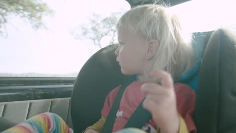 Cute-child-in-car-seat-stares-out-window-at-passing-countryside,-close-up