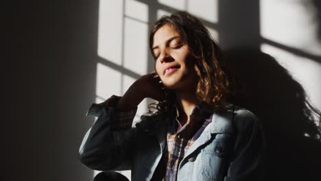 mujer de raza mixta relajada sentada y sonriendo en la sala de estar de una cabaña soleada