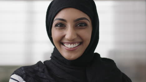 portrait of professional young muslim business woman looking at camera laughing cheerful wearing traditional headscarf in office background