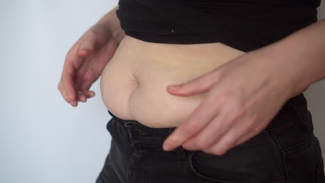 plump woman in black jeans touches fat belly