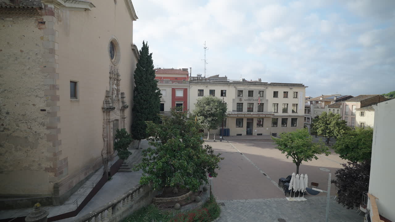 Vista amplia y apacible del ayuntamiento y la plaza de La Garriga, con árboles y edificios históricos bajo un cielo luminoso