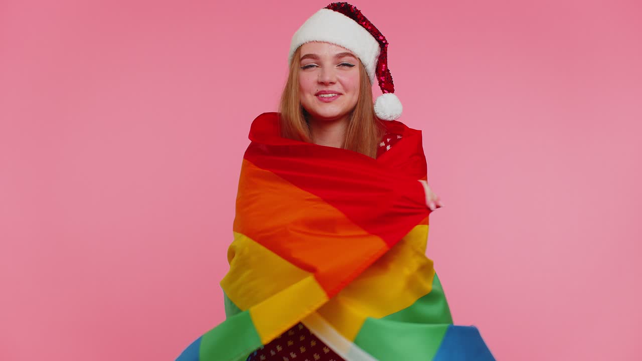 크리스마스 스웨터를 입은 소녀가 무지개  ⁇ 발과 포즈를 취하여 퍼레이드 관용 동성 결혼을 축하합니다.
