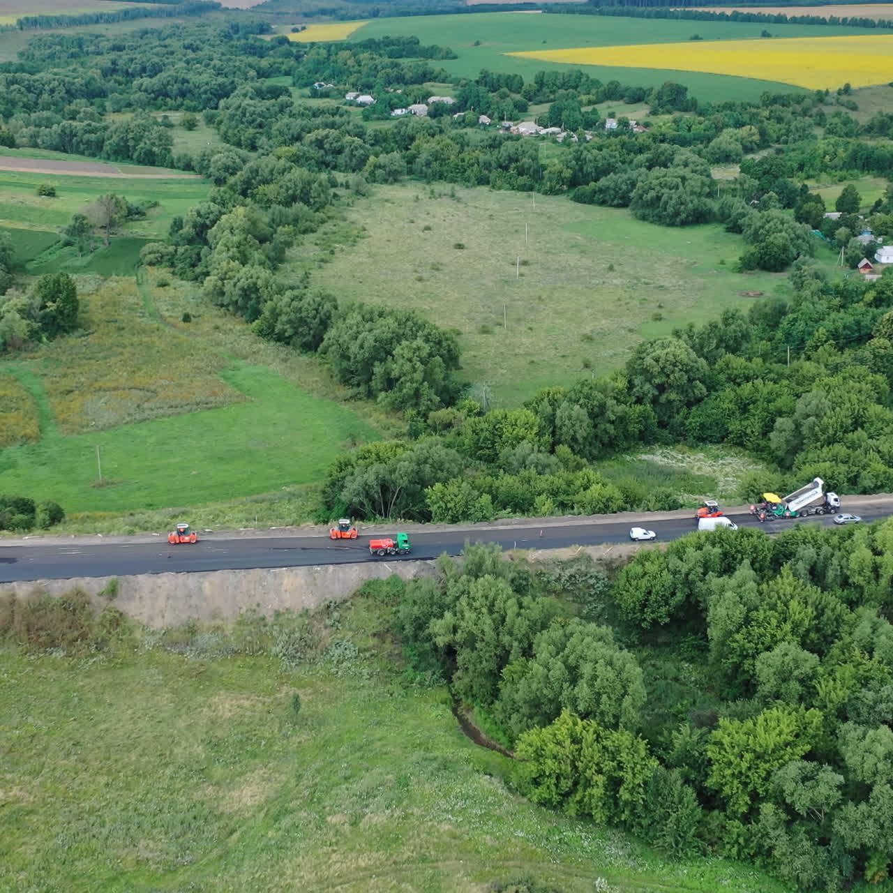 Aerial view of the road among nature. Side view of the highway with cars surrounded by green fields and forests. Machinery on the road during roadworks.