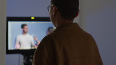 rear view of female film director watching performance of actors on monitor shooting movie or video in studio