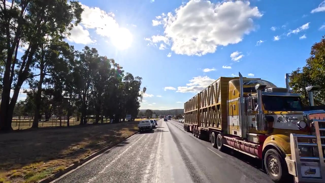 Una vista grandangolare da dashcam riprende veicoli che viaggiano lungo un'autostrada rurale australiana sotto un sole splendente