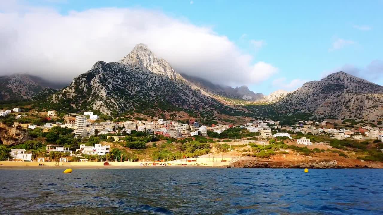 Vista panoramica di una città costiera con le montagne del Rif che si ergono dietro la costa nel Marocco settentrionale, con nuvole drammatiche sulle cime