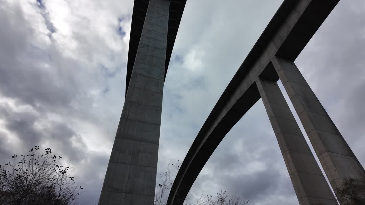 A towering concrete bridge rises above from a low-angle view under a cloudy sky