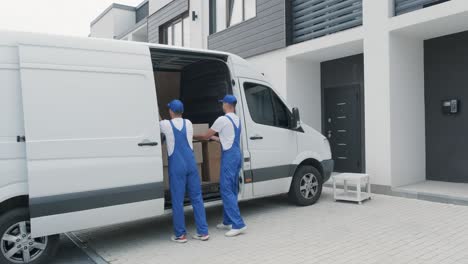 two young workers of removal company are loading boxes and furniture into a minibus